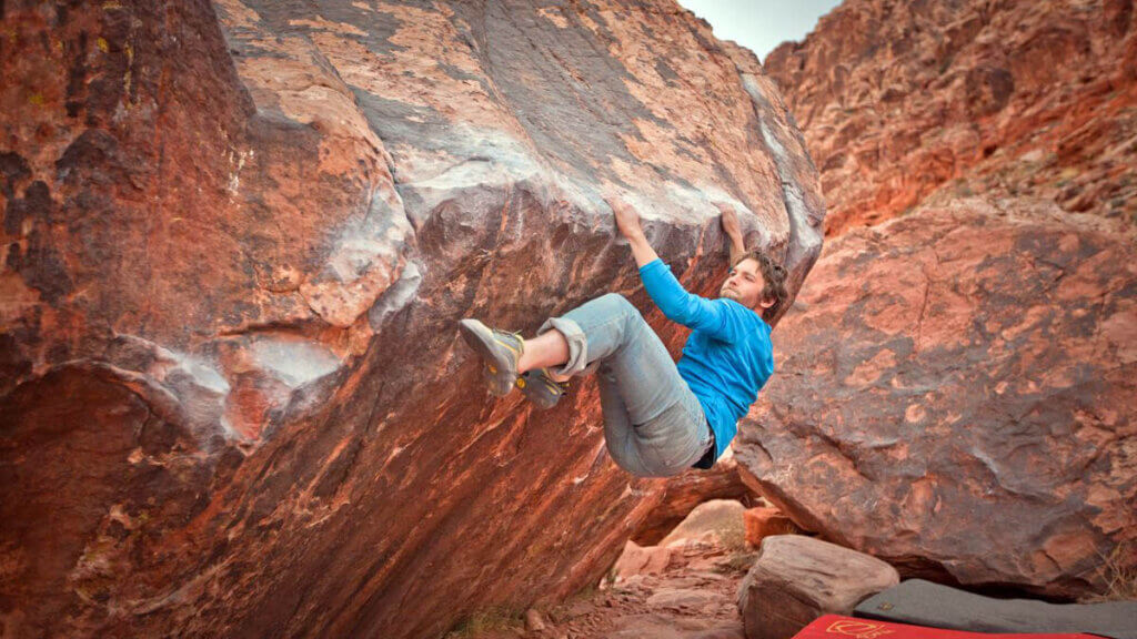 man hanging off red rock 