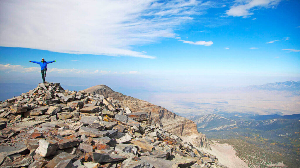 hiker celebrates after reaching the top of a mountain