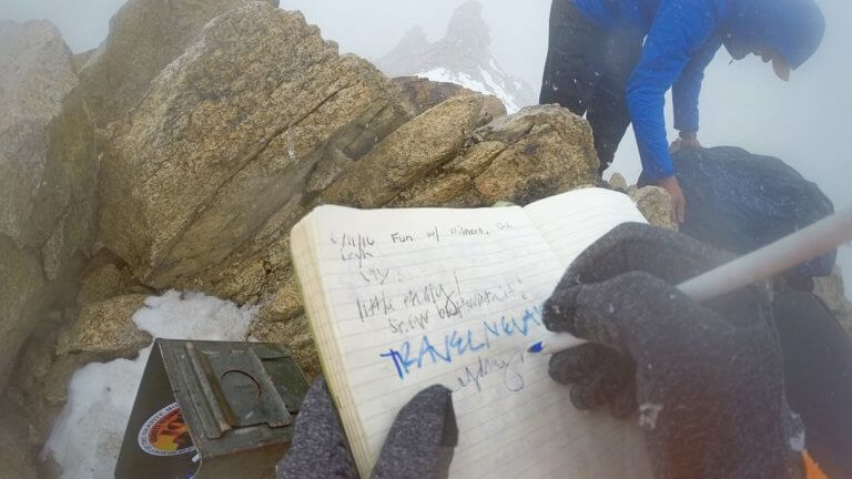 Person writing a notebook on top of boundary peak