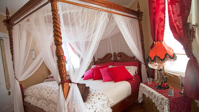 fancy bed with curtains and red pillows at the cobb mansion bed and breakfast