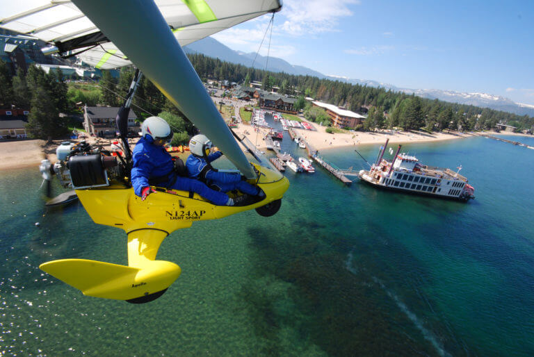 couple flying over lake tahoe beach in hang glider
