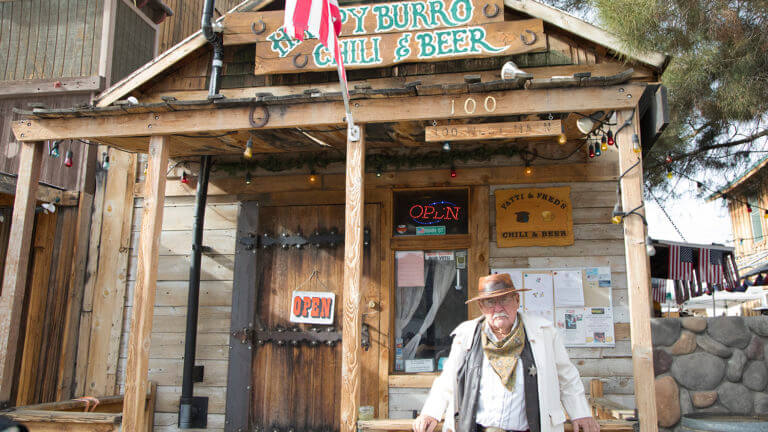 man dressed as a sheriff stands in front of the happy burro