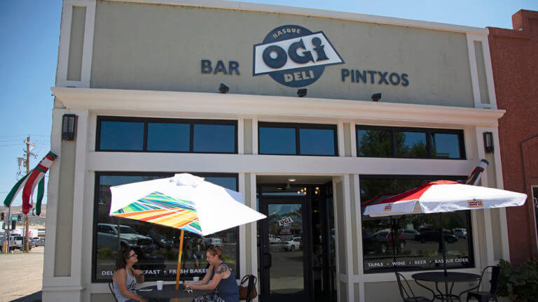 2 tables with umbrellas outside the ogi deli bar and pintxos