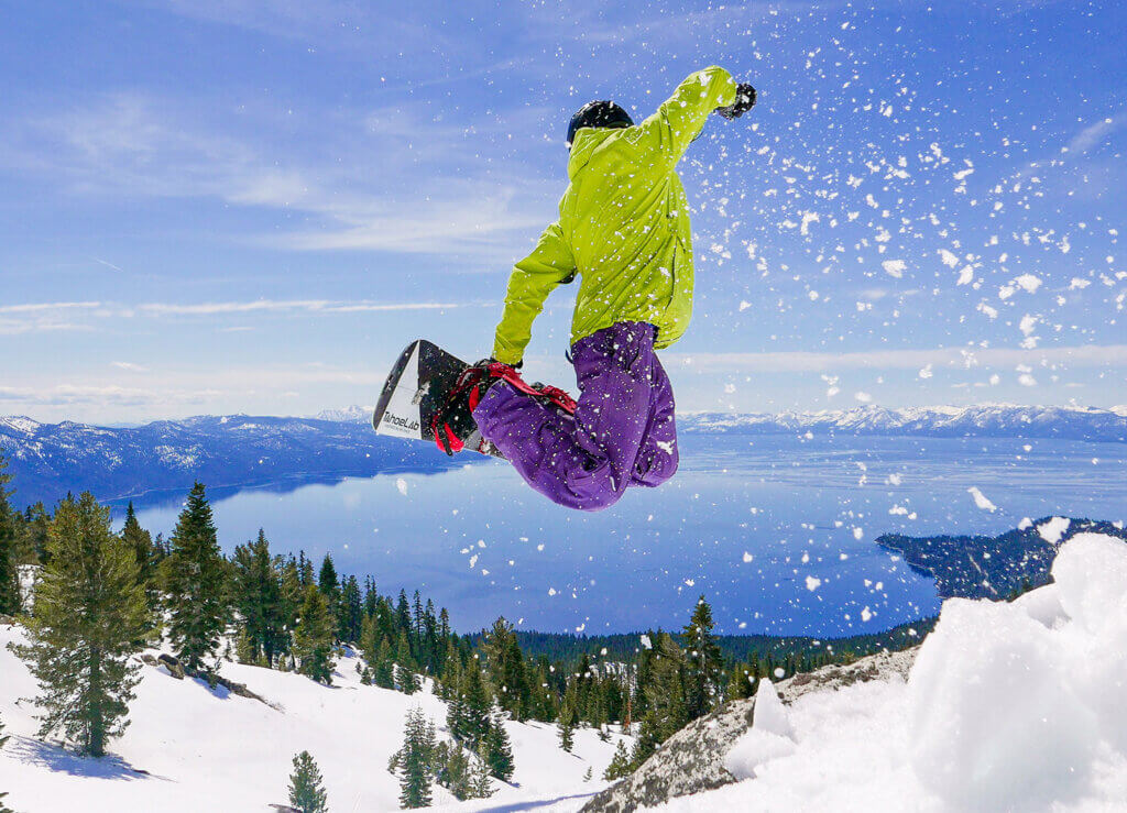 snowboarder going off a jump with lake tahoe in the background