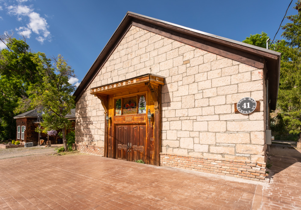 The stone/brick front to the Stone Church Lodge, not currently open to the public. A decorative set of wooden doors has paintings above it and decorative sconces. Brick groundwork surrounds the building on two sides, and a sign on the front reads "Tour Map 41 Eureka NV"