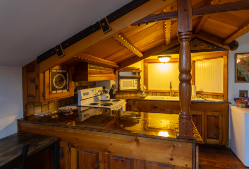 The kitchen to the Stone Church Lodge, shows an A-frame wooden ceiling, shining countertops, stove, microwave, sink, teapot, and refrigerator.
