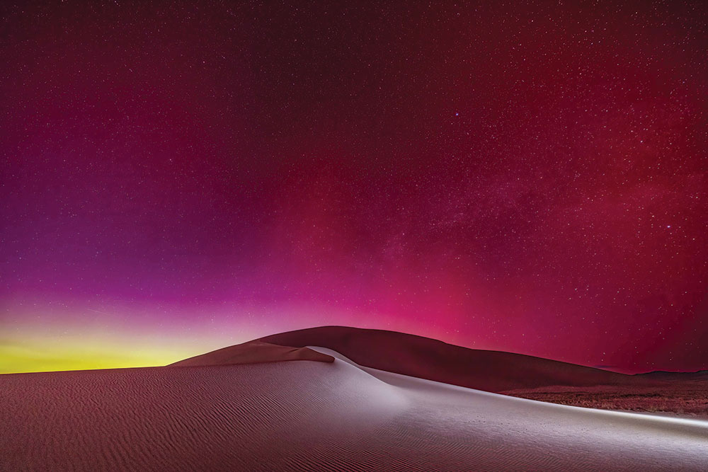 Tonopah sand dunes at night, with pink and green aurora borealis in the starry sky