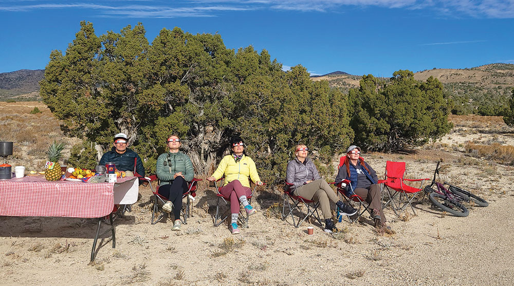 A group of people sitting near a picnic table in Sacramento Pass, enjoying the Annular Eclipse, while wearing special sunglasses