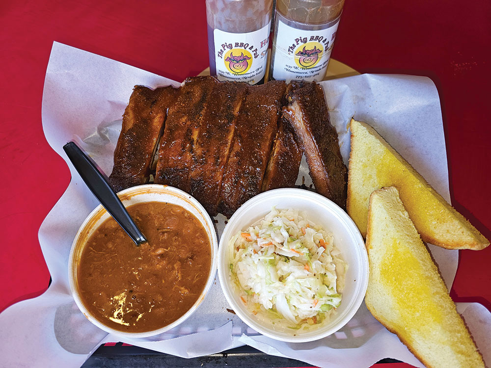 A plate of ribs, with bbq sauce, toasted bread, baked beans, and coleslaw