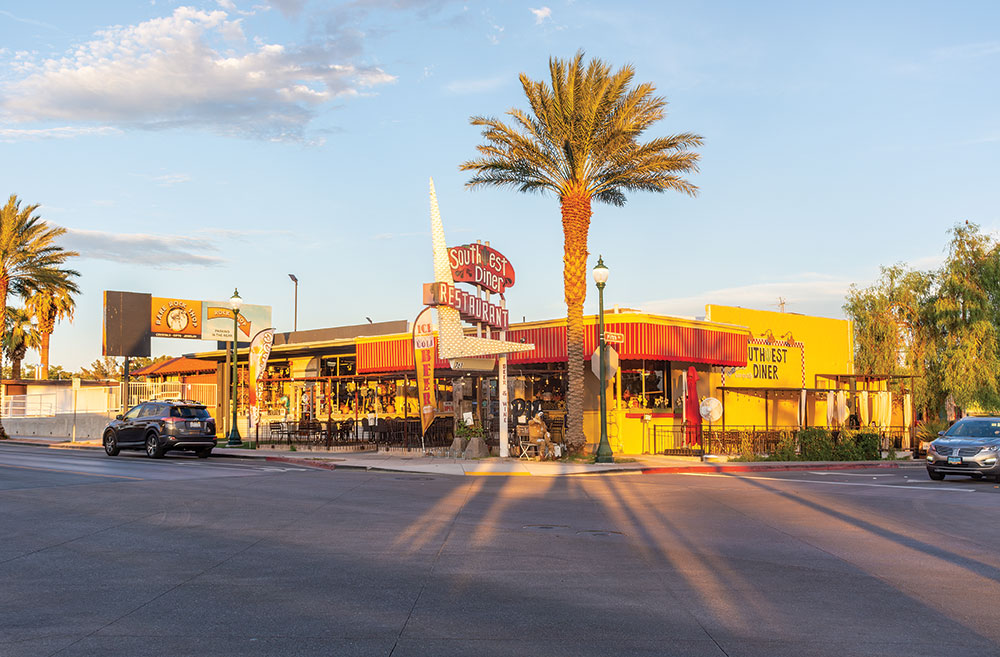 The Southwest Diner Restaurant in Boulder City, with palm trees (and other trees) all around, photo taken from across the street. Blue skies with clouds.