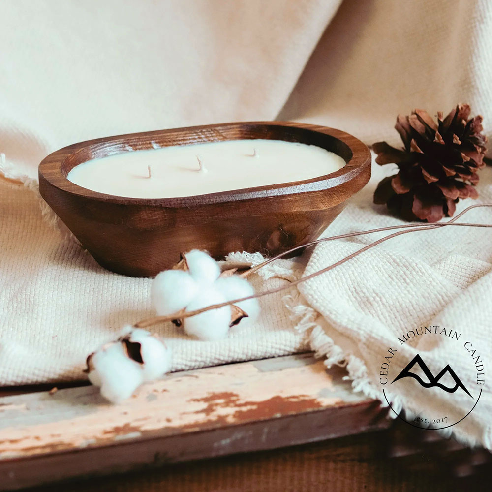 Cedar Mountain wooden candle with cotton plants and pine cone, sitting on a slab of wood.