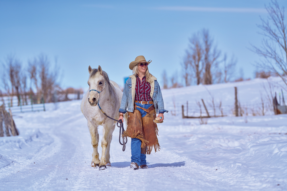 Woman walking on a snowy path with a horse.