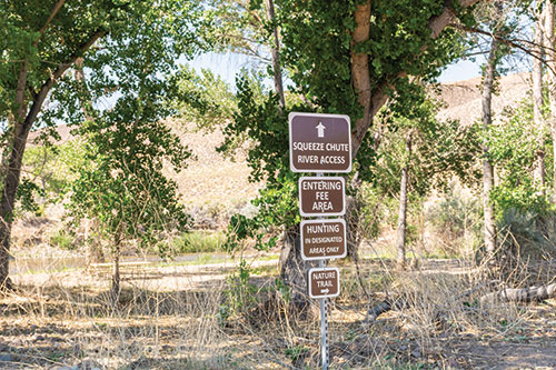 A series of signs reading: "Squeeze Chute River Access," "Entering Fee Area," Hunting in designated areas only," and "Nature Trail" (with an arrow pointing right)