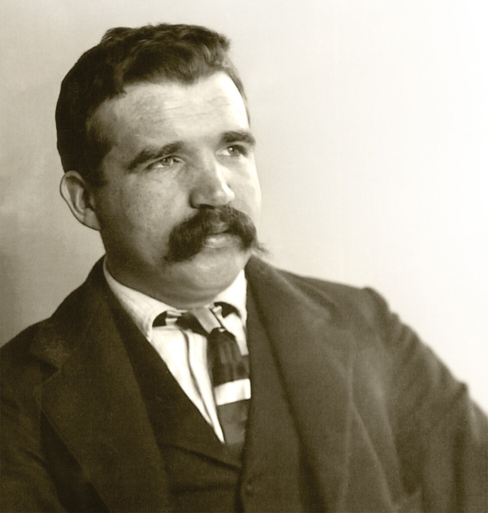 Diamondfield Jack Davis with a large mustache gazes sideways, wearing a suit and tie against a neutral background.