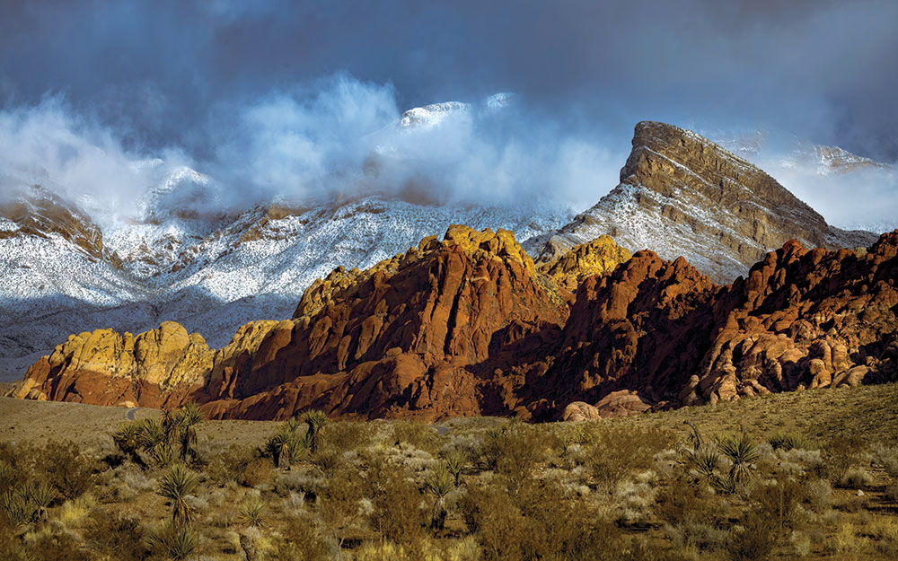 Red Rock Canyon, dusted in snow, with dramatic storm clouds obscuring part of the surrounding mountains
