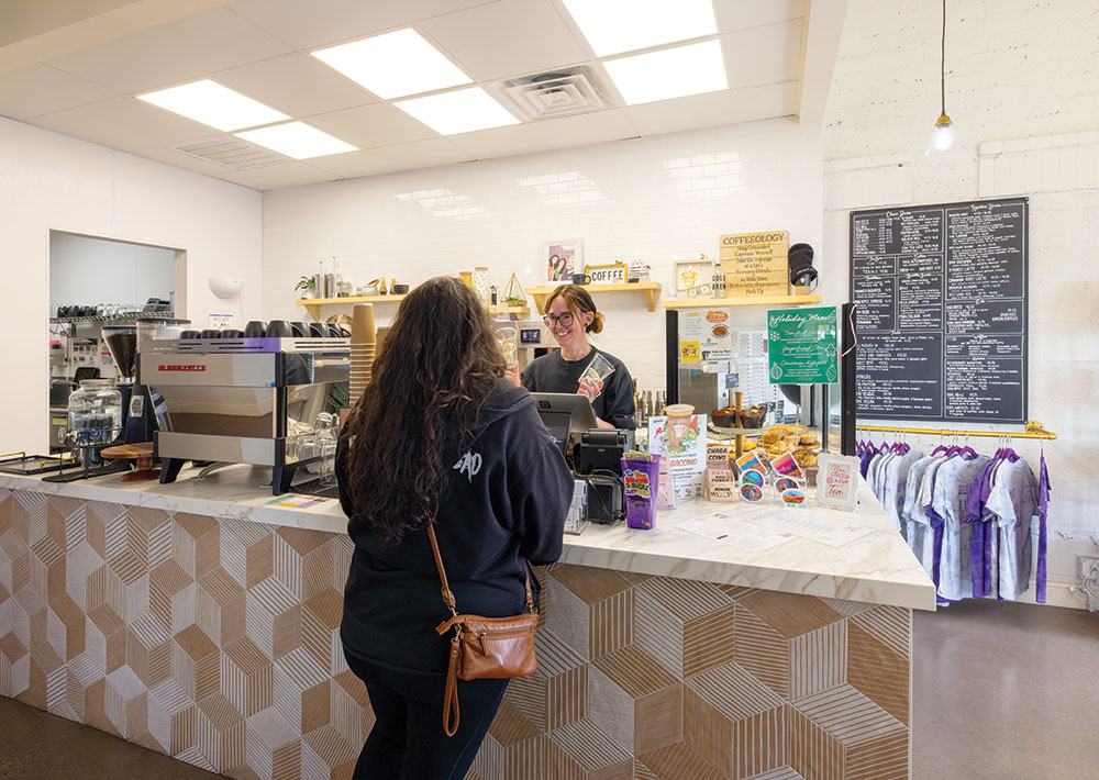 A woman orders coffee from a female barista at a coffee counter.