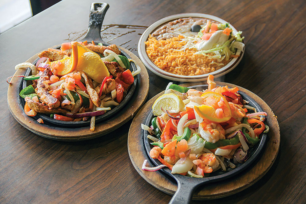 Chicken and shrimp fajita platters on a table, with a side plate of rice and beans and salad.