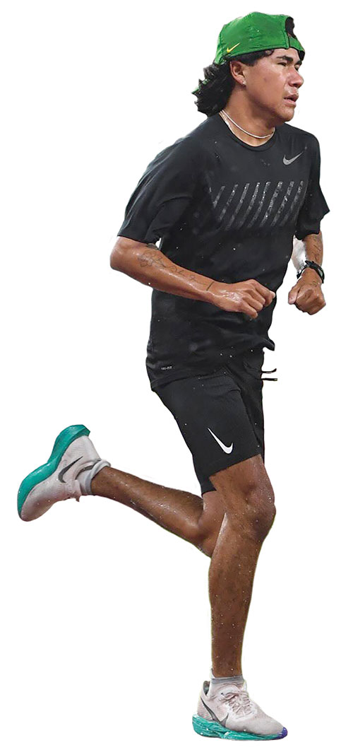 A young Native American man, Kutoven "Ku" Stevens, running while wearing black t-shirt and shorts and a green baseball cap