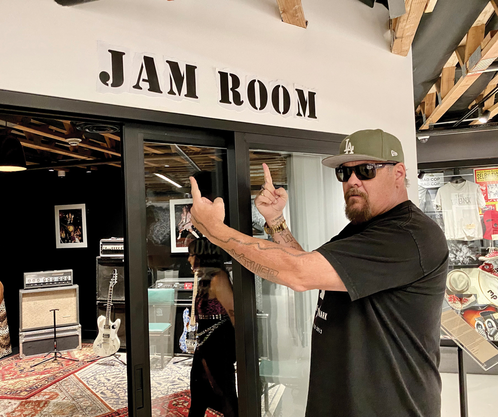 Fletcher from the band Pennywise pointing at a sign that says 'Jam Room' inside the Punk Rock Museum.