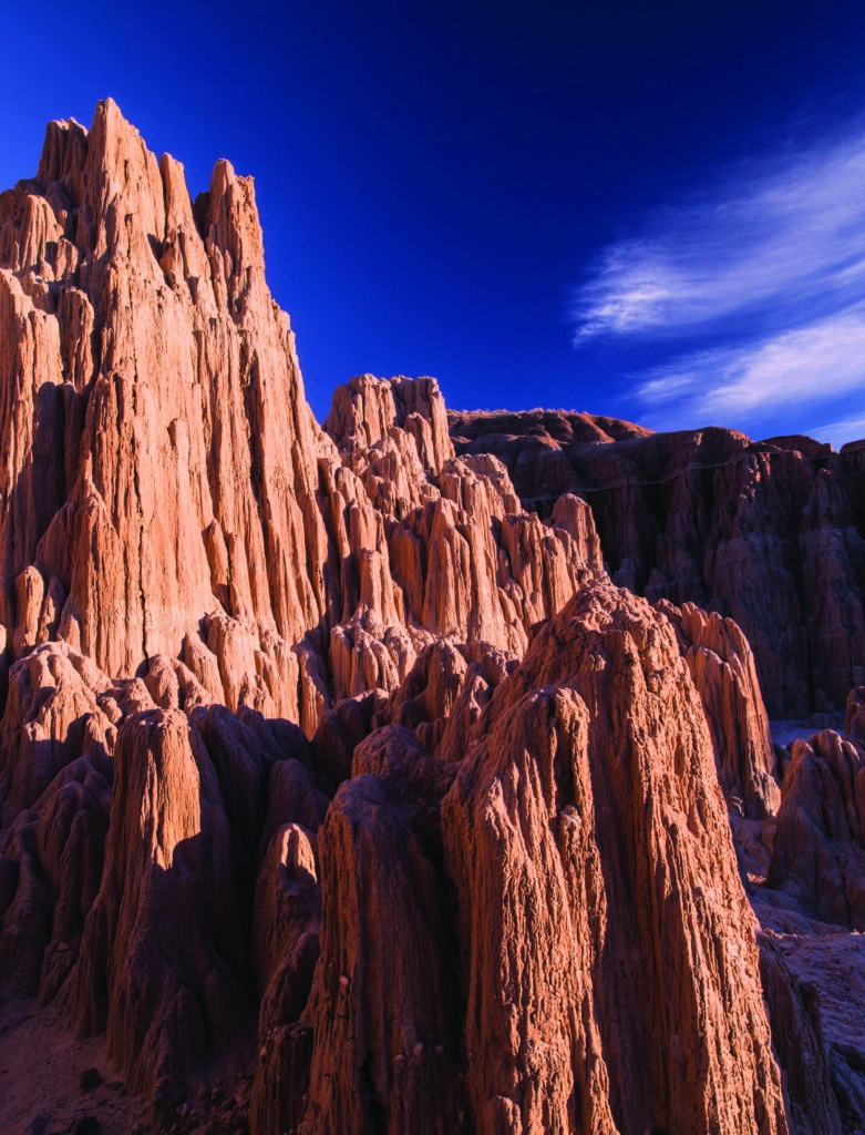 Rugged red rock formations tower under a deep blue sky with wispy clouds, creating a dramatic desert landscape.