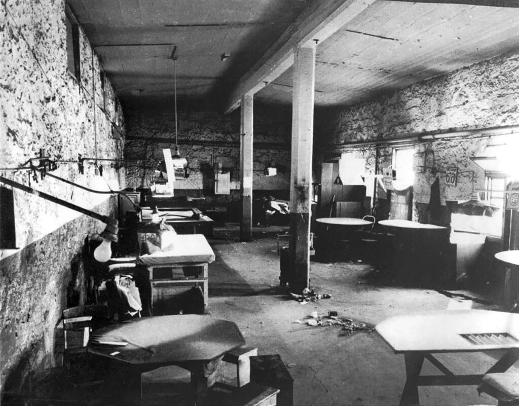 Worker assembles boards in spacious, industrial workshop with brick walls, support columns, and scattered worktables.