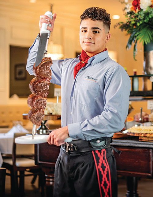 A server carrying a large skewer of meat at Churrasco Brazilian Steakhouse