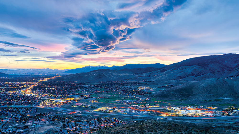 A photo from above, of Carson City at dusk, with buildings lit up and a dramatic cloudy sunset
