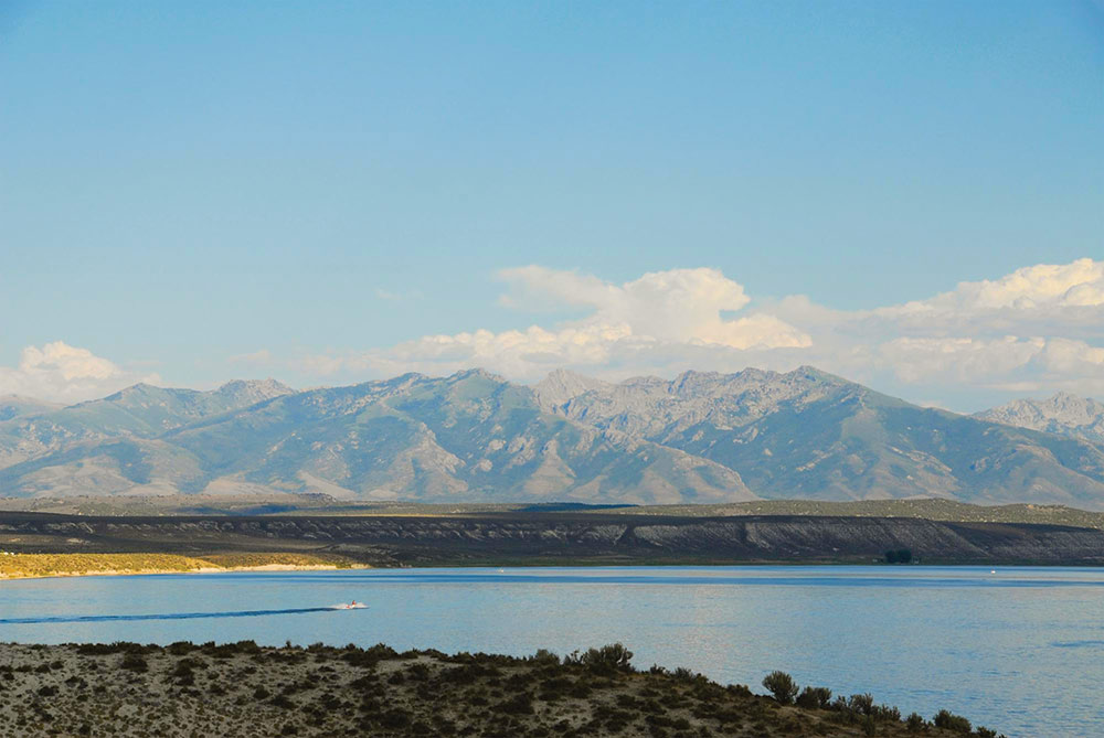 A jet ski rides across South Fork Reservoir. There are mountains in the distance, desert scrub along the shore, and puffy white clouds in a blue sky. Photo ©Nevada State Parks