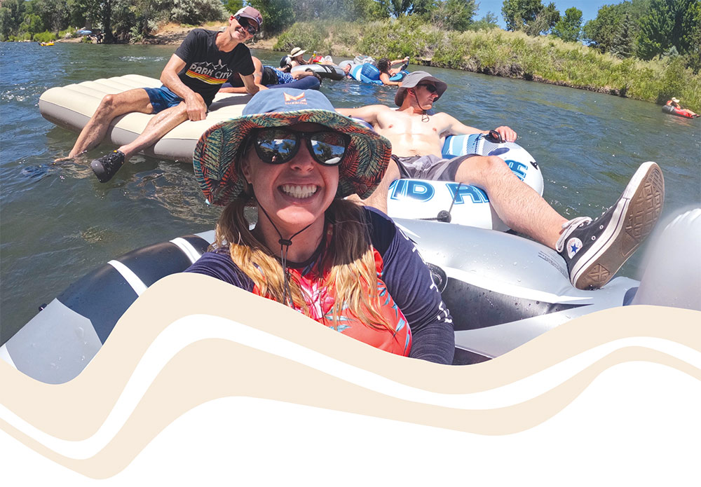 A young girl with two young men behind her, and others in the background, all on float tubes on a river.