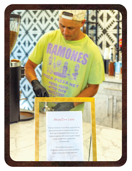 A barista preparing coffee, with a sign for a Maize/Corn Latte in the foreground