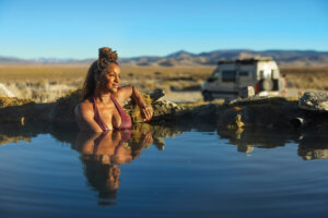 Woman soaking in Spencer Hot Springs with her van in the background.