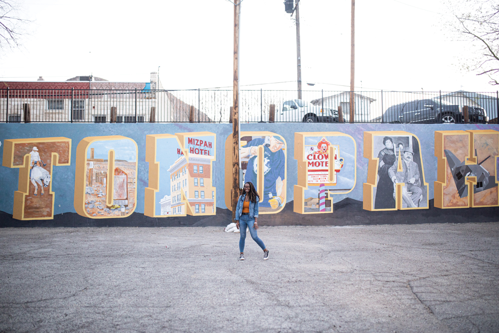 Woman standing in front of a mural spelling out Tonopah with pictures in the letters.