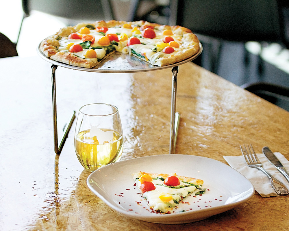 Pizza being served with a glass of wine.