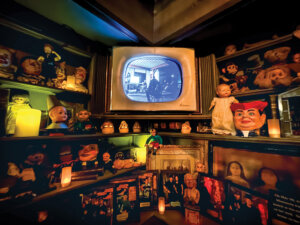 Inside Zak Bagans' Haunted Museum. Various doll heads line the shelves with an old tv in the center.