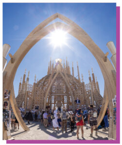 Wooden Structure at Burning Man with people walking in front of it.