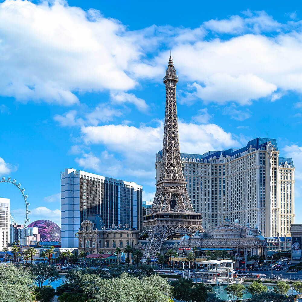 Las Vegas buildings, including an Eiffel Tower replica. Blue skies with puffy white clouds.