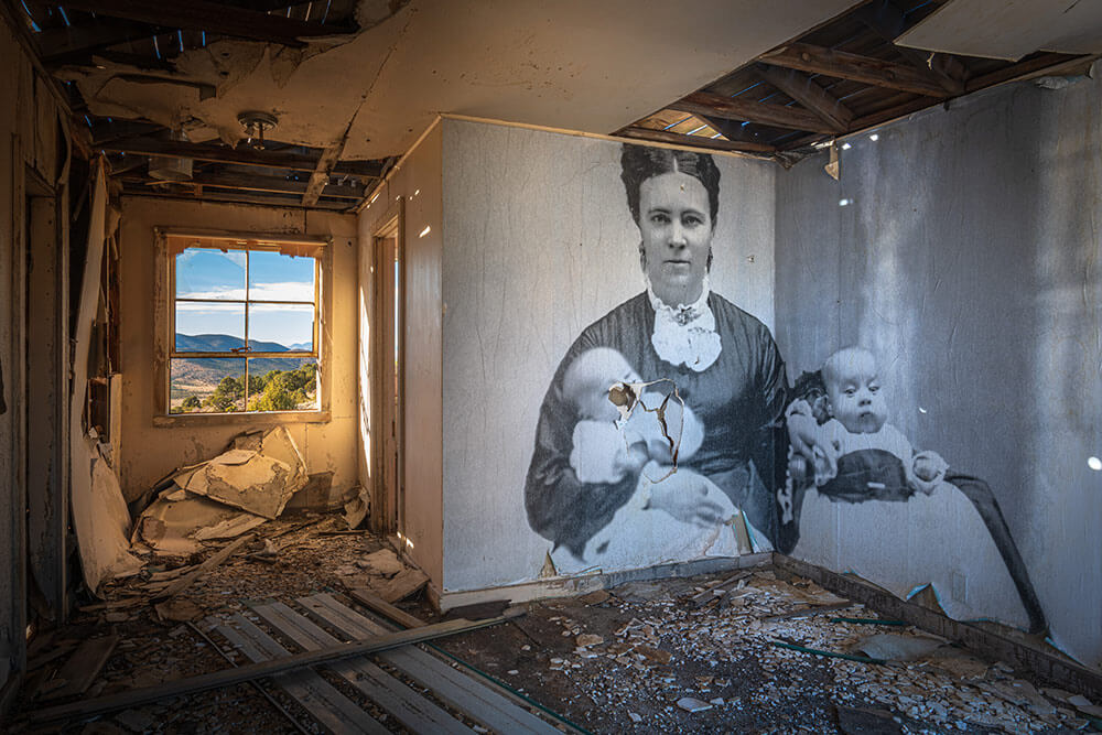 The inside of an old ghost town building, with a transferred black and white print of a woman with two babies on the walls.