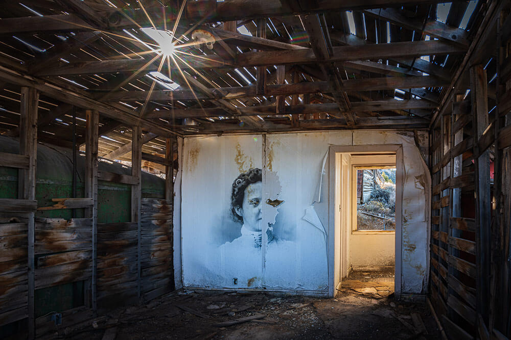 The inside of an old ghost town building, with a transferred black and white print of a woman on one wall.