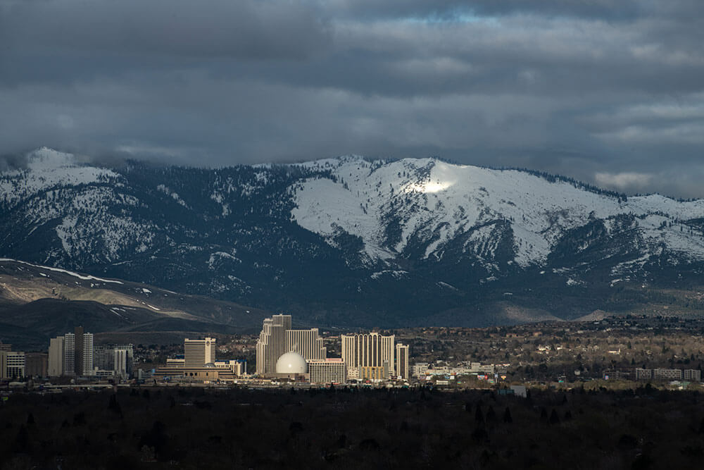 Buildings in downtown Reno, with snowy mountains and cloudy skies in the background.