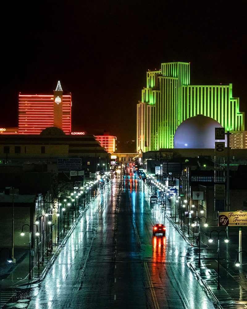 A wet street in Reno, shot from high up. Buildings are lit ad car lights are reflecting off the road.