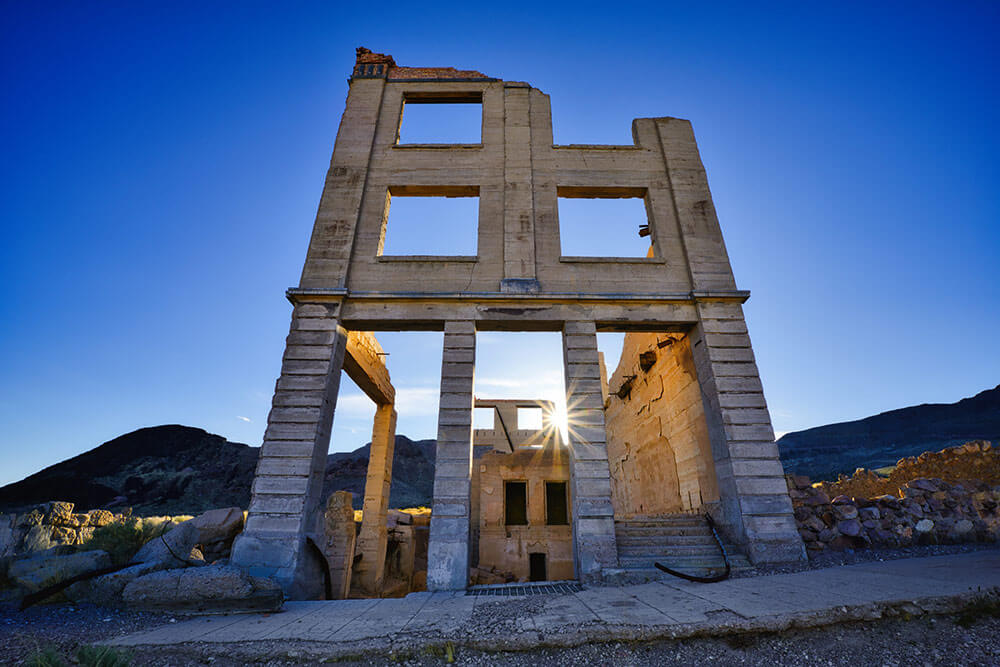 A stone/brick building in a ghost town, with a sunburst showing through and blue skies above.