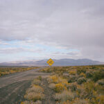 A desert scene with dirt road, sagebrush, mountains, clouds, and a sign that reads "OPEN RANGE."