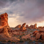 Red rocks jut out from the sagebrush-covered desert. Stormy clouds in the background.