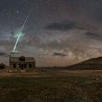 An abandoned building in the desert, at night. The sky is full our clouds, including a shooting one right above the building.