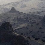 A desert scene with rocks jutting up from the ground, shot from above.