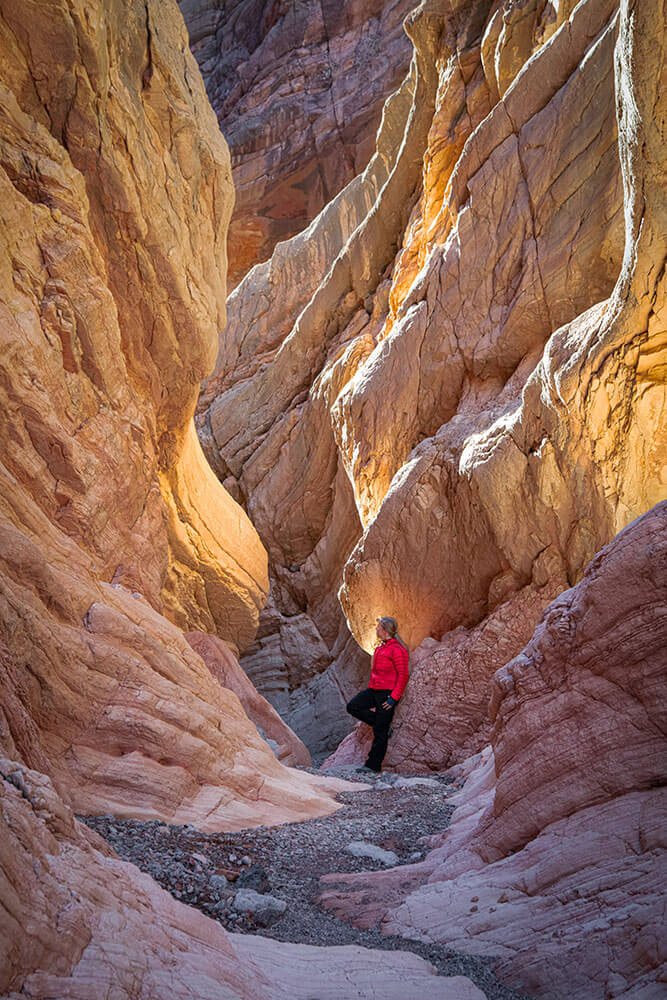 A person leans against a rock, in a tall rocky canyon.