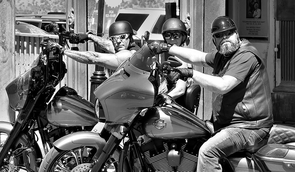 Black and white photo of people on motorcycles, scowling at the camera.