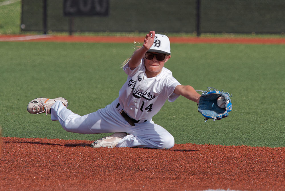 A young person in a baseball uniform dives to catch a ball.