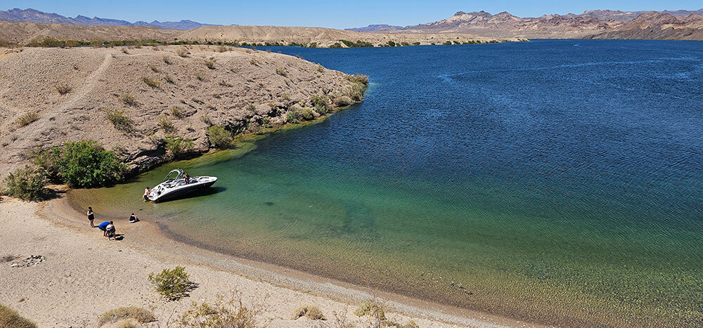 People with a small boat along the shoreline of a blue/green desert lake.