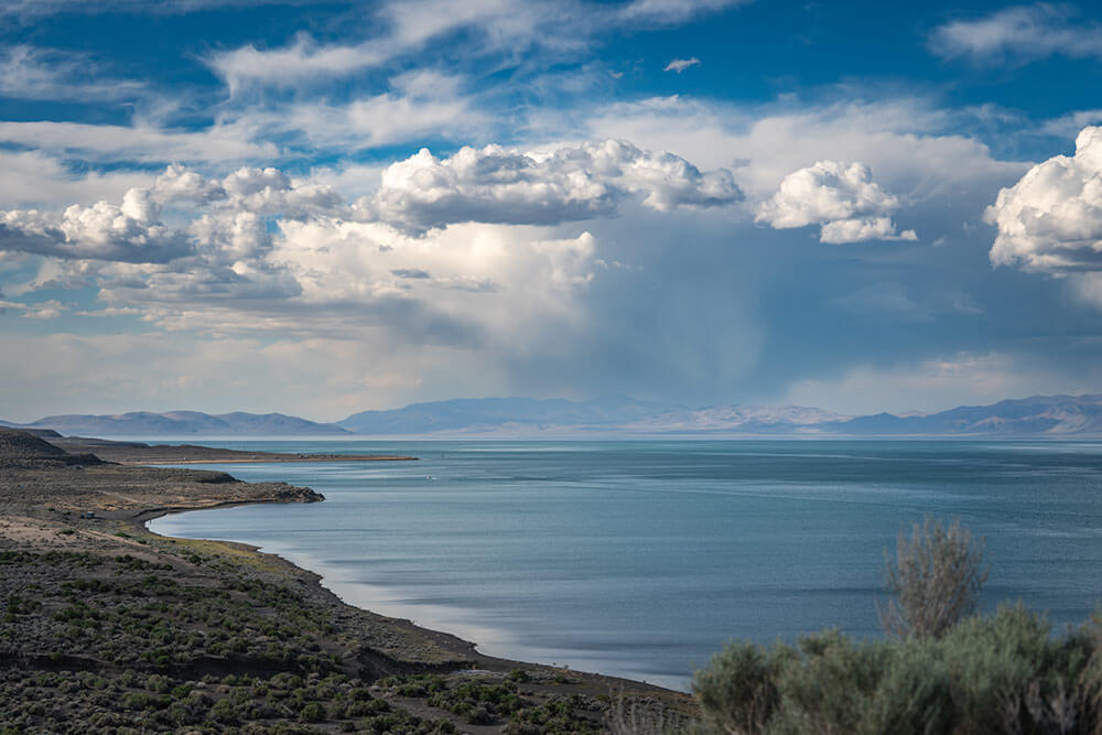 A desert lake with mountains in the background and cloudy blue skies.